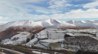 Göz kamaştırıcı bir manzara fotoğrafı karla kaplı dağlar ve dağınık bulutlu mavi gökyüzünün altındaki tarlalar, sakin bir kış manzarası yaratıyor..