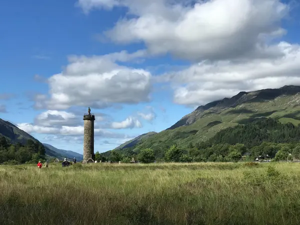 Çimenli tarlalar, tepeler ve bulutlu mavi gökyüzü ile çevrili uzun taştan bir anıtın yer aldığı manzaralı bir manzara..