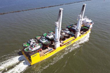 Rotterdam, Hollanda - 19 Mayıs 2024 - Rotterdam limanına yaklaşan birden fazla römorkör taşıyan eşsiz kaldırma kapasitesine sahip büyük bir geminin havadan görüntüsü