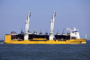 Rotterdam limanına yaklaşan birden fazla römorkör taşıyan eşsiz kaldırma kabiliyetine sahip büyük bir geminin hava görüntüsü.
