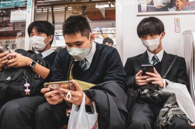 Metro 'da akıllı telefonlar kullanan üç Japon öğrenci.