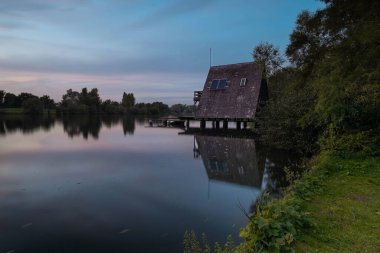 Güneş panelleri olan ahşap bir kabin, gölün kenarlarında durmaktadır. Yumuşak suda yansıtılır. Gökyüzü ise günbatımında maviden yumuşak pembelere dönüşür.