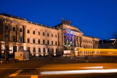 Braunschweig Sarayı 'nın aydınlatılmış mimarisi ve önplandaki binicilik heykeliyle, geçen trafikten gelen ışık izleriyle çekilen çarpıcı bir gece fotoğrafı..