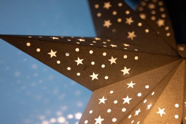 Kesik yıldız ve nokta desenli parlayan bir kağıt yıldız fenerinin yakın çekimi, yumuşak bir arkaplanda sıcak bir şekilde parlıyor. Noel, kış tatili ve ev dekorasyonu için ideal..