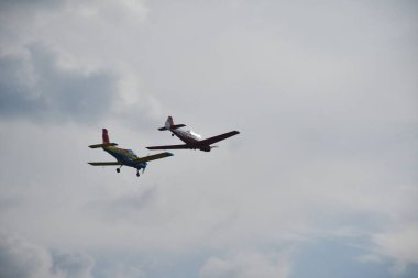 Bir havacılık olayı sırasında bulutlu bir gökyüzünün altında iki hafif akrobatik uçak gevşek bir düzende uçar..
