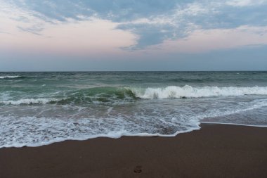 Tatlı okyanus dalgalarının kumlu kıyılara çarptığı, doğal güzellikte huzurlu bir deniz manzarası yaratan pastel bir gün batımı..