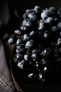 Yakın plan, taze, olgun siyah üzümler su damlacıklarıyla, koyu ahşap bir yüzey üzerinde