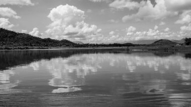 Nehrin ahşap bir teknedeyken çekilmiş siyah beyaz bir fotoğrafı. Nehir kıyısının yansıması görünüyor.. 