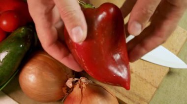 Erkek elleri ahşap tahtada taze dolma biberi soğan, domates ve bıçakla tutar. Çan biberi canlı renk ve doku gösterir, sebzelerin yanında biber ise güzelliği ön plana çıkarır. Sağlıklı ev yemeği kavramı.