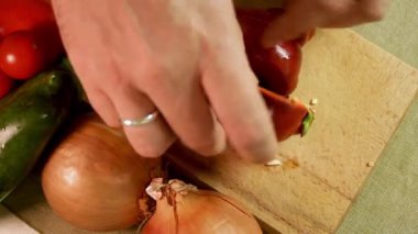 Erkek eller, kırmızı dolma biberden soğan ve biber dolu tahta kesme tahtasına tohum döker. Kırmızı dolma biber canlı bir renk ve doku gösteriyor. Sağlıklı beslenme ve taze ev yemeği kavramı.