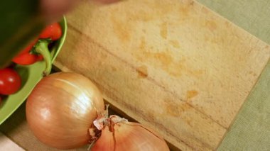 Erkek elleri, yeşil dolma biberi diğer sebzelerle çevrili tahta kesme tahtasıyla keser. Yeşil dolma biber canlı renk ve doku gösteriyor. Sağlıklı ev yemeği kavramı.