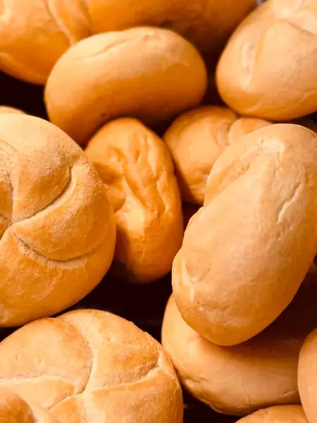 Kırsal bir düzende üst üste dizilmiş taze, yumuşak ekmek rulolarının yakın çekimi, altın-kahverengi kabuklarını ve yumuşak dokusunu sergiliyor, fırın ya da yemek fotoğrafçılığı için mükemmel..