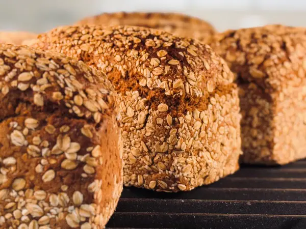 Soğutma rafında sergilenen altın kabuklu taze pişmiş yulaf ekmeği desenli yüzeyin yakın çekim görüntüsünü sunuyor..