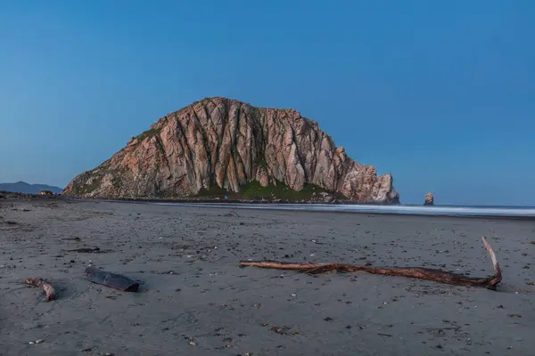 Morro Rock at sunrise, in Morro Bay, California.Beach in foreground littered with shells and driftwood. Pacific ocean to one side.