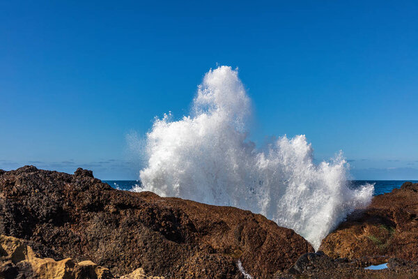 Wave crashing against rocks at Point Lobos Nature Preserve, Monterey, California. Spray thrown high into the air. Pacific ocean and clear blue sky in the background.