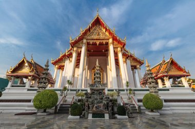 Bangkok, Tayland 'daki Wat Suthat Tapınağı' na giriş. Ön bahçedeki süs eşyası. Her iki taraftaki diğer binalar; mavi gökyüzü ve yukarıdaki bulutlar. 