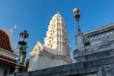 White, Bangkok, Tayland 'daki Wat Ratchapradit Sathit' e saldırmış. Bitişikteki binadan ışık ve taş korkuluklar görünüyor. Mavi gökyüzü tepemizde. 