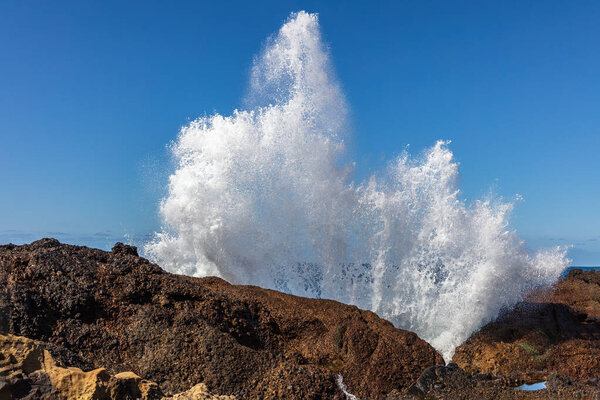 Wave crashing against rocks at Point Lobos Nature Preserve, Monterey, California. Spray thrown high into the air. Pacific ocean and clear blue sky in the background.