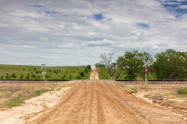 Cloud County, Kansas 'tan kalkan toprak çiftlik yolu. Uzakta yeşil alanlar ve ağaçlar var. Bulutlu mavi gökyüzü tepemizde. 