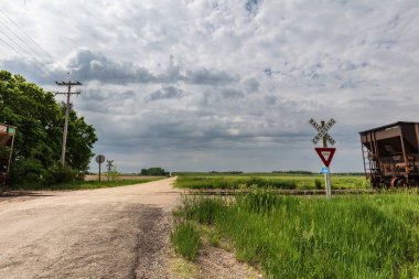Kansas, Cloud County 'deki kırsal çiftlik yolu. Demiryolu raylarına doğru gidiyor, demiryolu vagonu görünür durumda. Ağaçlar, ötesinde yeşil alanlar. Bulutlu gökyüzü.