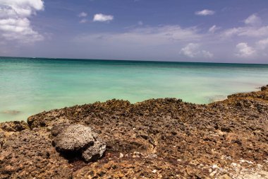 Aruba adasındaki Rocky plajı. Körfezdeki zümrüt yeşili su ufka kadar uzanıyor. Bulutlu mavi gökyüzü tepemizde.