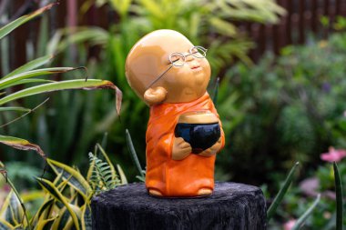 Bangkok, Tayland 'daki Wat Apson Sawan Tapınağı bahçesindeki ağaç kütüğünde gözlüklü Buddist keşişin küçük renkli heykeli.. 