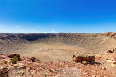 Winslow, Arizona yakınlarındaki Barringer Meteor Krateri 'nde gözle görülür bir gözlem platformu var. Eskimiş kayalar, ön planda çöl bitkileri. Gökyüzü açık mavi. 