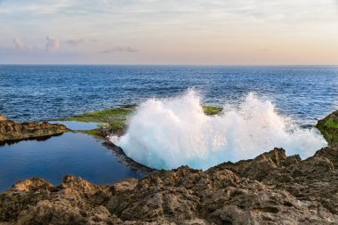 Dalgalar, Endonezya, Bali, Nusa Lembongan sahilindeki Devil 's Tear' da kayalıklara çarpıyor. Öndeki uçurumun tepesindeki su havuzu. Arka planda mavi okyanus. Gökyüzü ve bulutlar uzakta. 