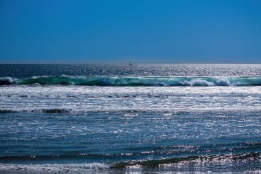 Huntington Sahili 'nden Pasifik Okyanusu manzarası kıyıya doğru hareket eden dalgalar, uzaktaki yelkenli. Mavi gökyüzü. 
