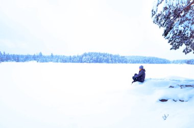Donmuş bir göl kenarındaki yalnız bir yürüyüşçünün atmosferik kış görüntüsü. Soğuk, vahşi doğa ve yalnızlık kavramı..