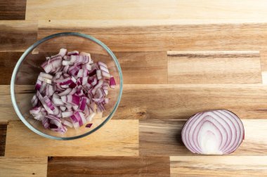 Tahta bir yüzey üzerinde kırmızı soğanın yanında bir kase doğranmış kırmızı soğan. Tarifler, yemek blogları veya dizayn şablonları için fotokopi alanı olan düz bir ahşap yüzey..