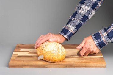 Tahta kesme tahtasının üzerinde yuvarlak bir ekmek dilimleyen biri. Tarifler, bloglar ve mutfak tasarımı için uygun Rustik ahşap kesim tahtası arka planı.