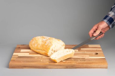 Bir somun ekmeği tahta kesme tahtasıyla dilimleyen biri. Tarifler, bloglar ve mutfak tasarımı için uygun Rustik ahşap kesim tahtası arka planı.