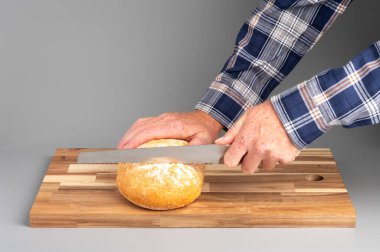 Tahta kesme tahtasının üzerinde yuvarlak ekmek dilimleyen biri. Tarifler, bloglar ve mutfak tasarımı için uygun Rustik ahşap kesim tahtası arka planı.