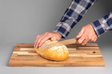 Bir somun ekmeği tahta kesme tahtasıyla dilimleyen biri. Tarifler, bloglar ve mutfak tasarımı için uygun Rustik ahşap kesim tahtası arka planı.