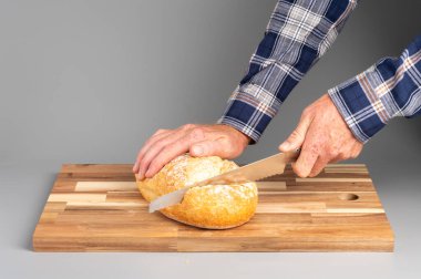 Bir somun ekmeği tahta kesme tahtasıyla dilimleyen biri. Tarifler, bloglar ve mutfak tasarımı için uygun Rustik ahşap kesim tahtası arka planı.