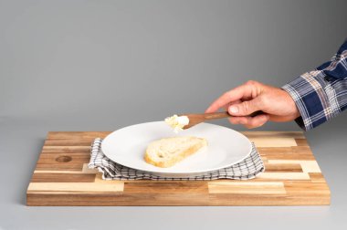 Tahtayla beyaz bir tabakta bir dilim ekmeğe tereyağı süren bir el. Tarifler, bloglar ve mutfak tasarımı için uygun Rustik ahşap kesim tahtası arka planı.