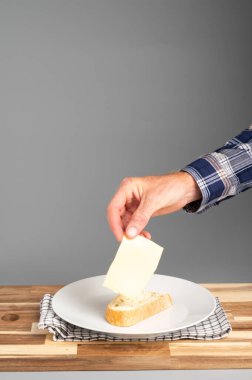 Tabaktaki bir parça ekmeğe peynir koyan bir el. Tarifler, bloglar ve mutfak tasarımı için uygun Rustik ahşap kesim tahtası arka planı.