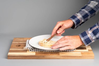 Tahta bir tahtanın üzerinde bıçakla ekmeğe tereyağı süren bir insan. Tarifler, bloglar ve mutfak tasarımı için uygun Rustik ahşap kesim tahtası arka planı.