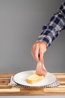 Peynirli ekmek dilimine jambon koyan bir insan. Tarifler, bloglar ve mutfak tasarımı için uygun Rustik ahşap kesim tahtası arka planı.