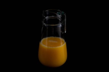Siyah arka planda portakal suyu dolu bir cam sürahi.