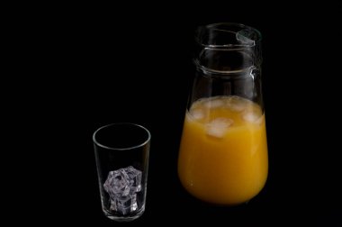 Portakal suyu ve buzla dolu bir cam sürahi, buz küpleriyle birlikte, siyah bir arka planda.