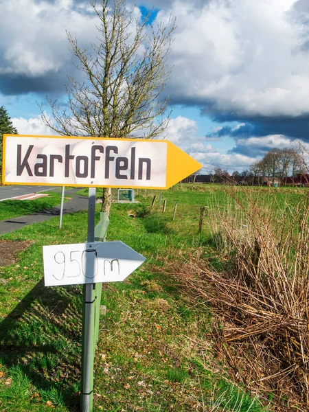 Doğu Friesland 'da mavi gökyüzü ve büyük beyaz bulutları olan bir köy yolunda patates satışına işaret eden manzara..