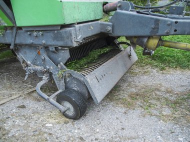 Partial view of the PTO spring tines and pickup roller of a baler on a gravel surface after intensive use. clipart