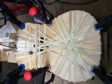 Akustik gitar gövdesinin üst kısmının lastik bant ve vida kıskaçlarıyla yapıştırılmasının üst görüntüsü.