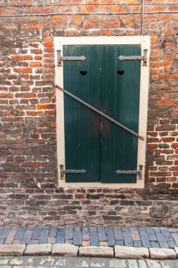 Yıpranmış tuğla duvarda kilitli panjurları olan eski bir pencerenin ön görüntüsü.