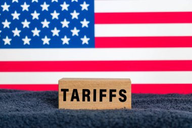 Arkadaki Amerika bayrağında tahtadan bloklar üzerine tarifeler yazıyor.