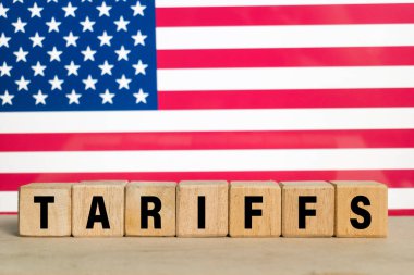 Arkadaki Amerika bayrağında tahtadan bloklar üzerine tarifeler yazıyor.