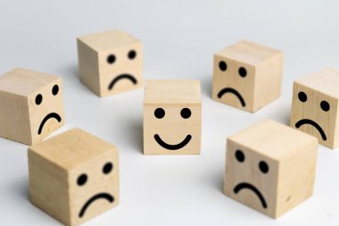 Beyaz arka planda izole edilmiş ahşap blokta hüzünlü yüz ifadelerinin arasında mutlu bir yüz.