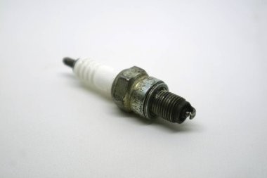 A used spark plug with a ceramic insulator and metal threads is positioned on a white background.